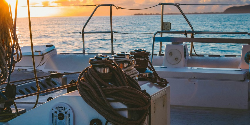 Deck of a cruise boat with ropes attached, sunset in the background and distant shores.